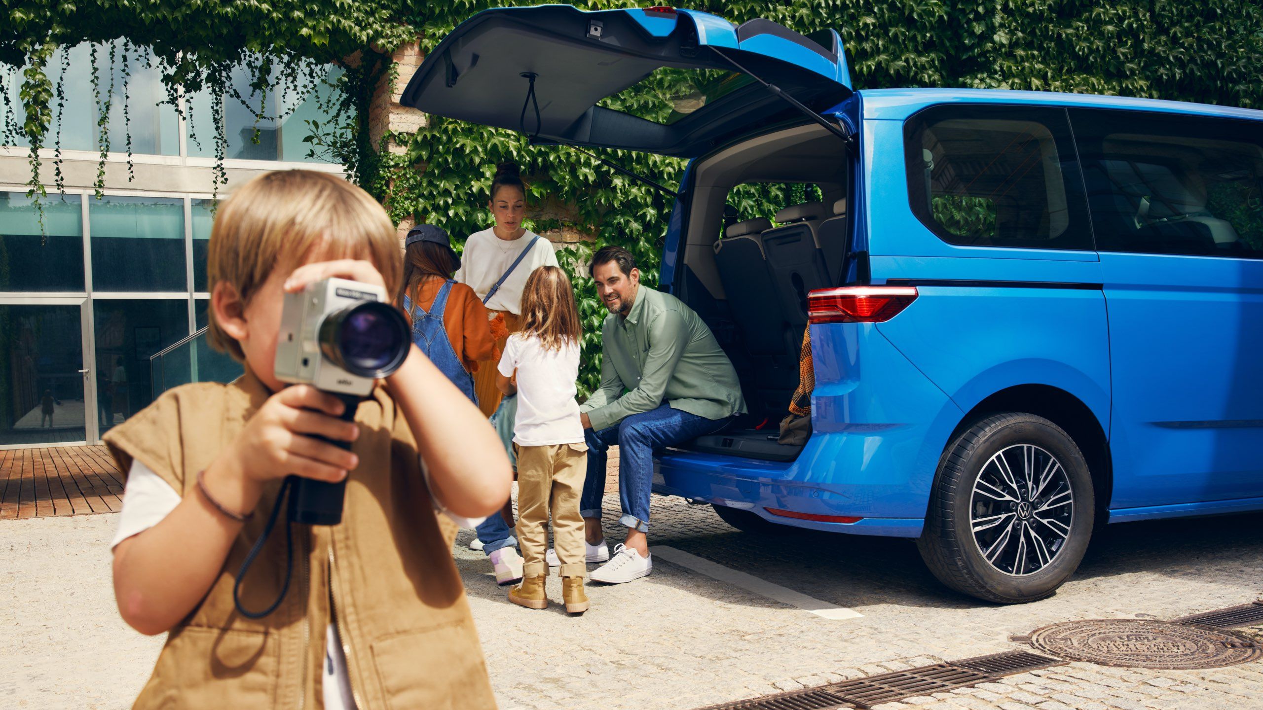 Eine Familie steht neben der geöffneten Heckklappe des neuen VW Multivan T7 2021.
