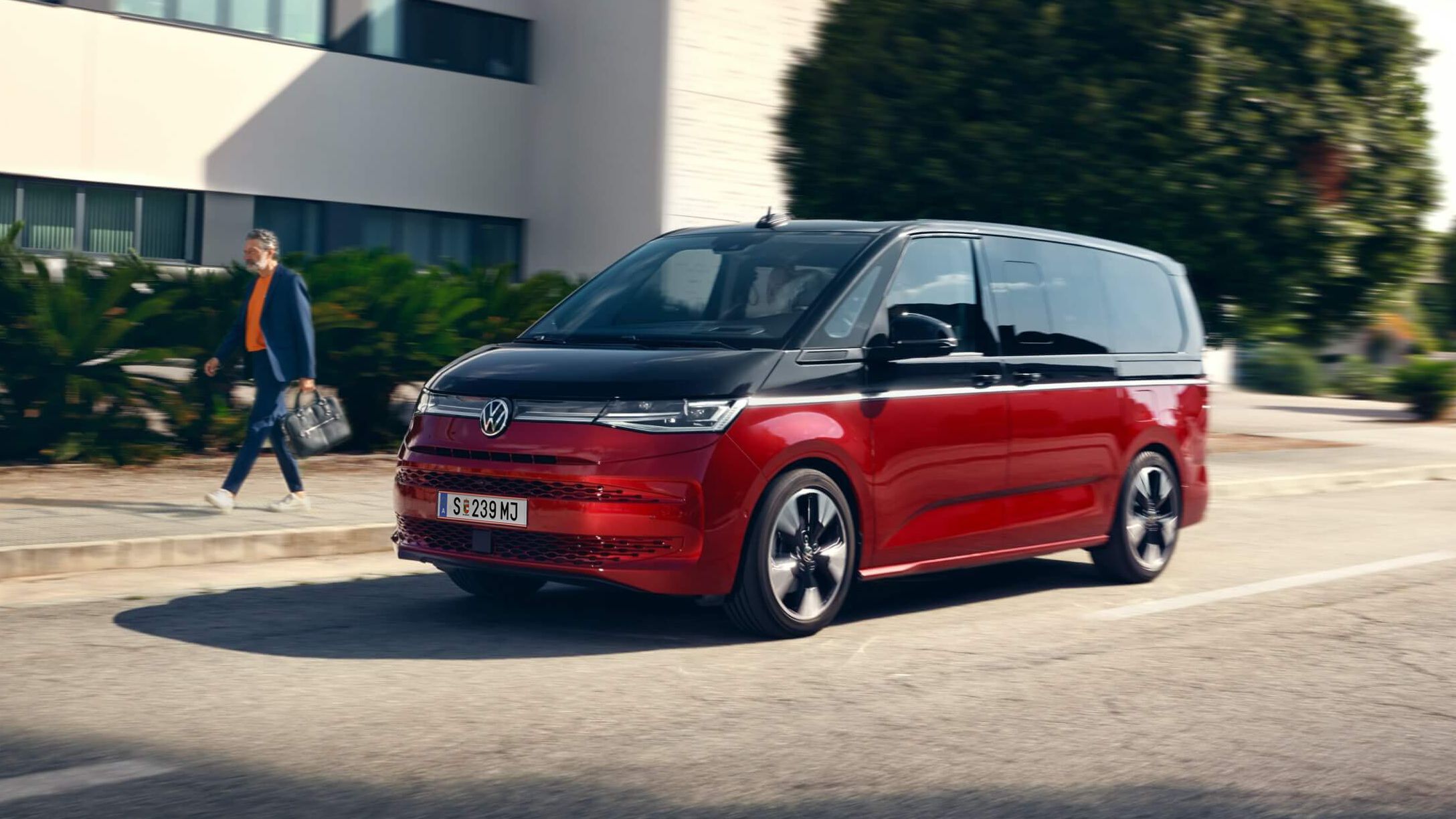 Der neue VW Multivan Style T7 fährt auf einer Straße neben einem Mann. 