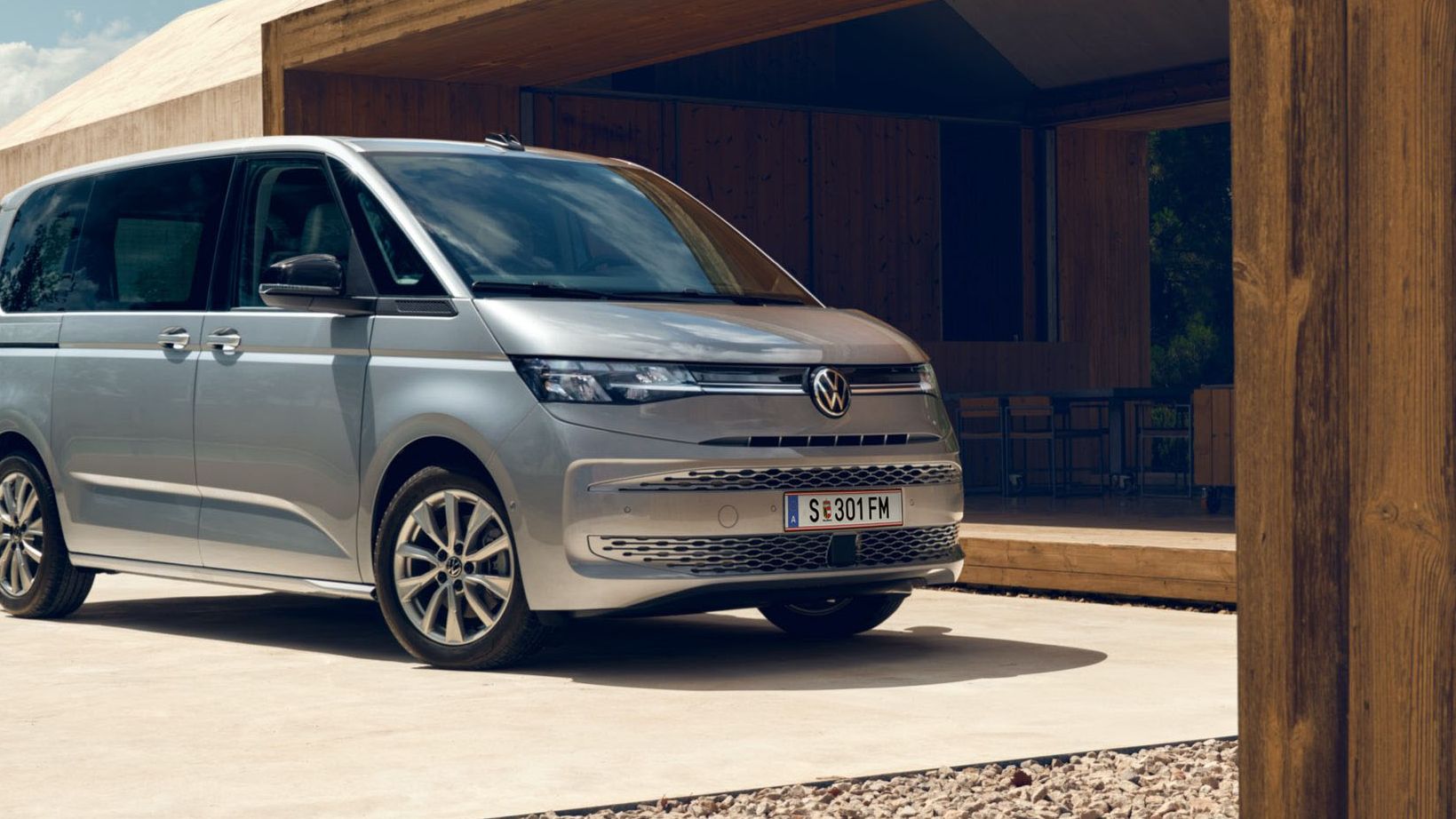 Zwei Männer mit Sporttaschen laufen vor einem neuen silbernen VW Multivan T7 2021.
