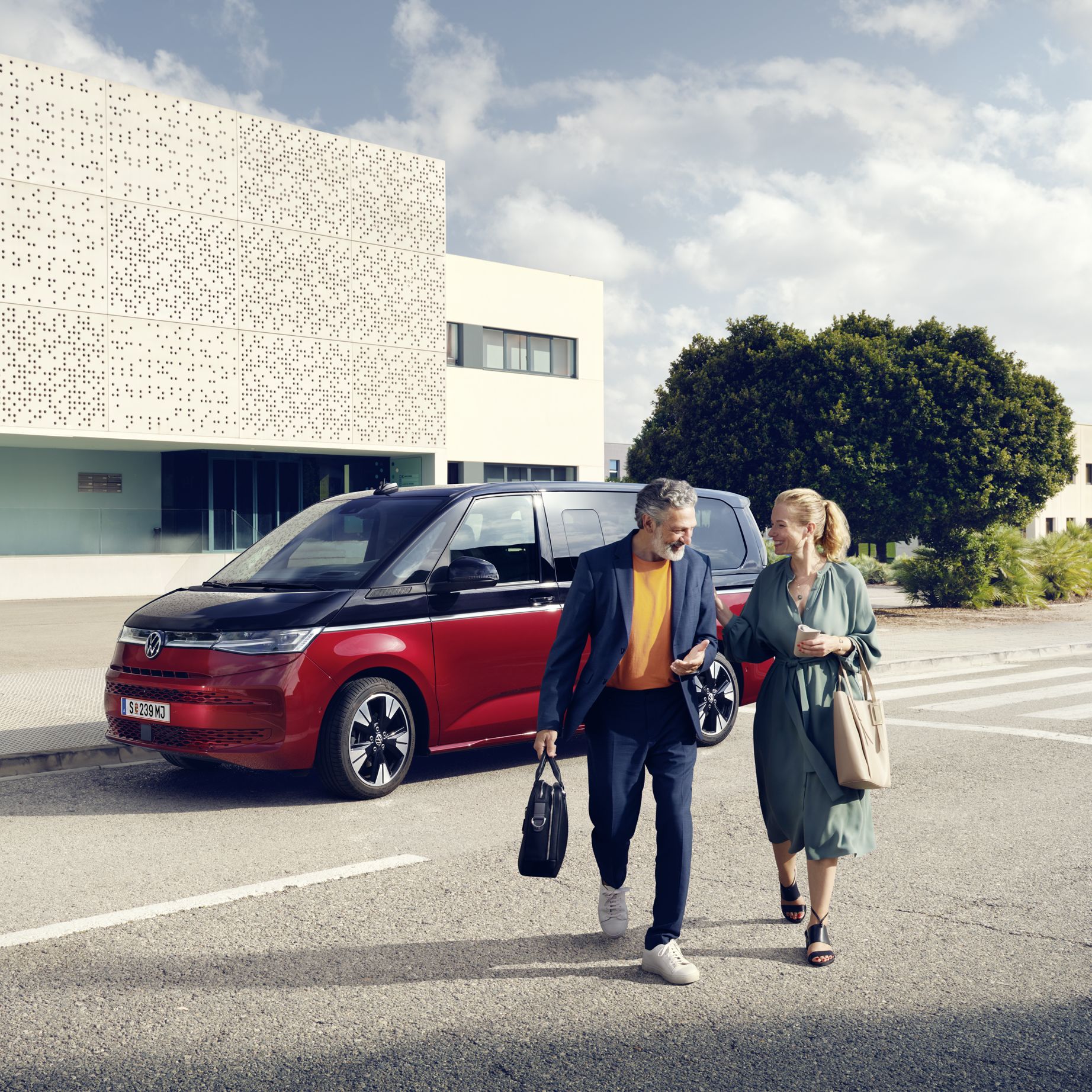 Ein Paar läuft vor einem neuen VW Multivan T7 2021 Style. 
