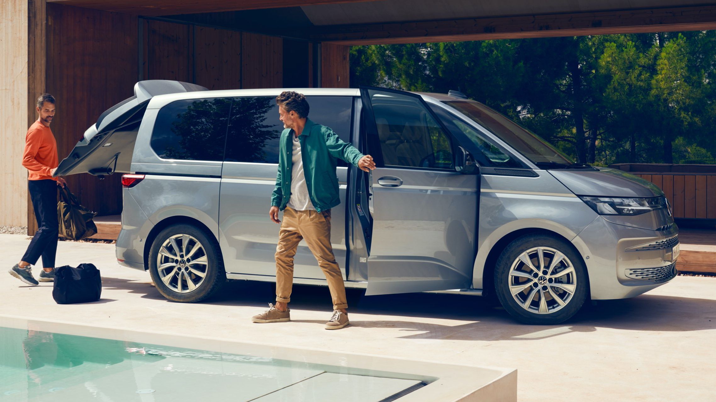 Zwei Männer stehen mit Gepäck neben dem neuen VW Multivan T7 2021.