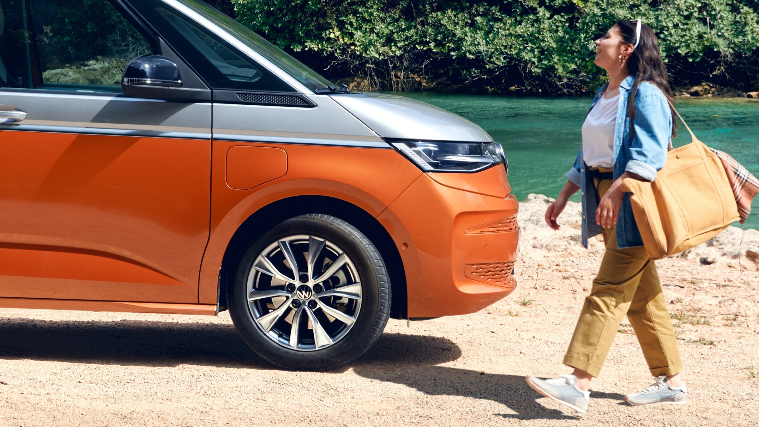 Eine Frau läuft neben dem neuen VW Multivan T7 2021 Energetic in zweifarbiger Lackierung.
