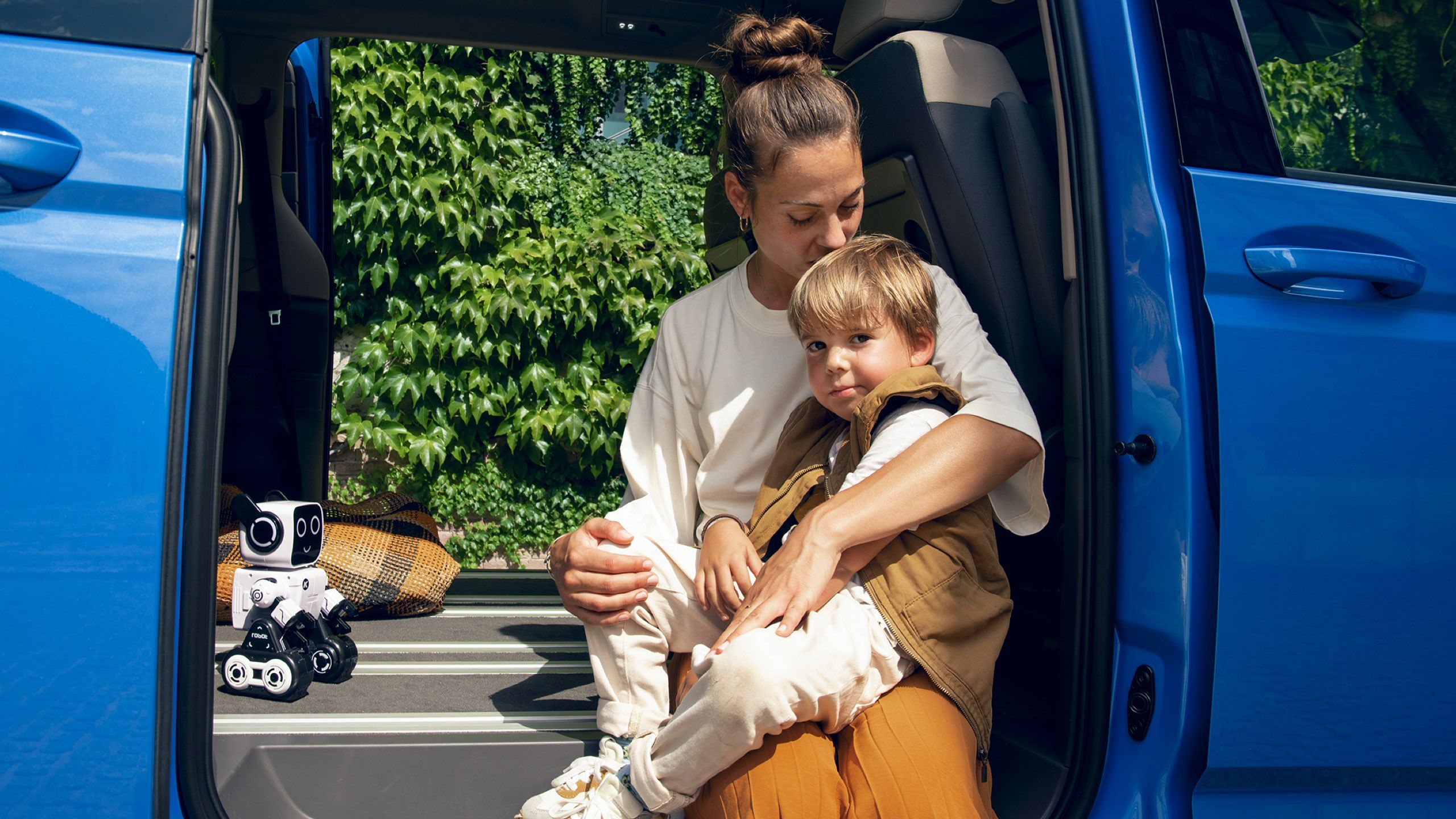Eine Mutter sitzt mit ihrem Sohn im Rahmen einer offenen Schiebetür des neuen VW Multivan T7 2021.